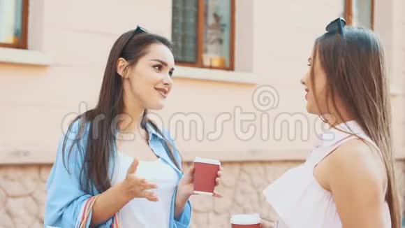 两个有魅力的年轻女人正在夏天的街道上聊天喝咖啡快关门复制空间4K视频的预览图