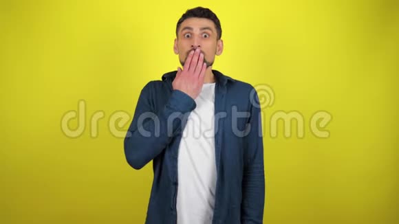 一个穿着蓝色衬衫和白色T恤的年轻人看着相机把手伸进嘴里非常惊讶视频的预览图