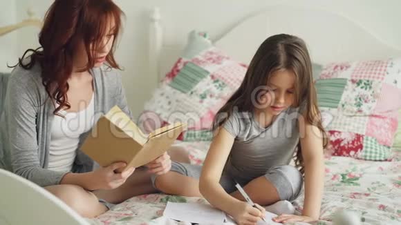 年轻的母亲帮助她可爱的小女儿做小学作业爱妈妈看书爱女孩视频的预览图