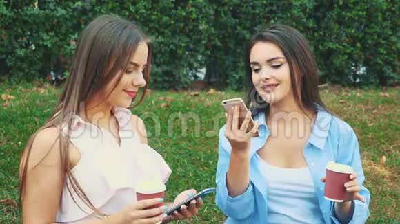 购物后的女孩坐在公园的长凳上其中一个在打电话另一个坐在旁边视频的预览图