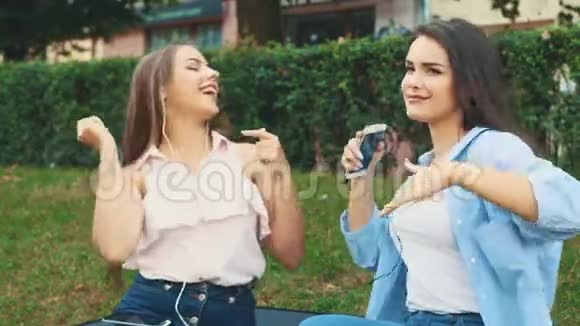 两个漂亮的女孩在公园里用耳机听音乐复制空间4K视频的预览图