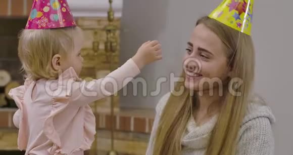 年轻的白人女人和戴着派对帽的小可爱女孩在家玩得很开心漂亮的宝贝想把妈妈帽子摘下来视频的预览图