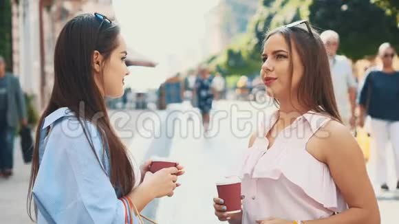 两个有魅力的年轻女人正在一条夏天的街道上喝咖啡快关门复制空间4K视频的预览图