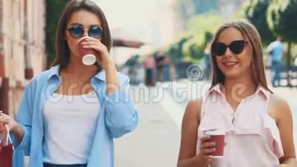 两个有魅力的年轻女人在一条带着咖啡杯的夏日街道上散步和交谈快关门复制空间4K视频的预览图