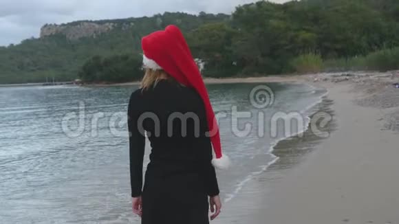 戴着圣诞帽走在海边的年轻女子视频的预览图