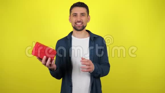 一个穿着白色T恤的年轻人手拿着礼物扔出一个盒子看着相机微笑着黄色的背景视频的预览图