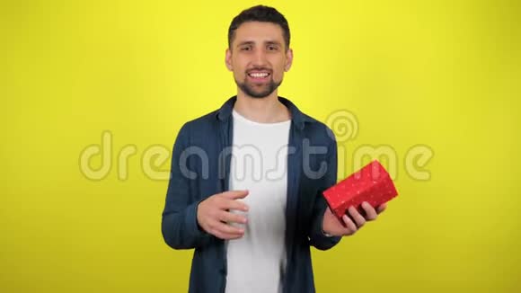 一个穿着白色T恤的年轻人手拿着礼物扔出一个盒子看着相机微笑视频的预览图