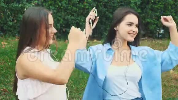 两个漂亮的女孩在公园里用耳机听音乐快关门复制空间4K视频的预览图
