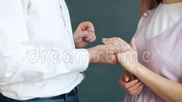 爱的男人把订婚戒指戴在女孩身上她的手指站在灰色的背景上视频的预览图