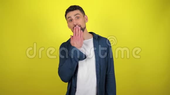 一个穿着蓝色衬衫和白色T恤的年轻人把手放在嘴唇上看着相机视频的预览图