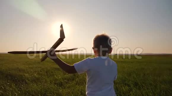 快乐的孩子穿着一件白色T恤带着一架玩具飞机在日落背景下跑过一片田野幸福的概念视频的预览图