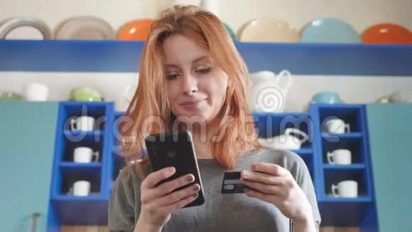 漂亮的红发女孩用智能手机和信用卡在网上商店购物购买空气视频的预览图