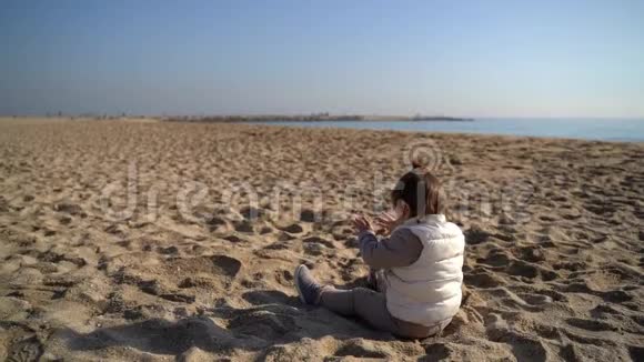 在寒冷多风的日子里孩子在沙滩上坐在海岸线上玩沙子西班牙视频的预览图