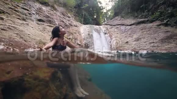 美丽的年轻女子坐在森林中原始的瀑布流视频的预览图