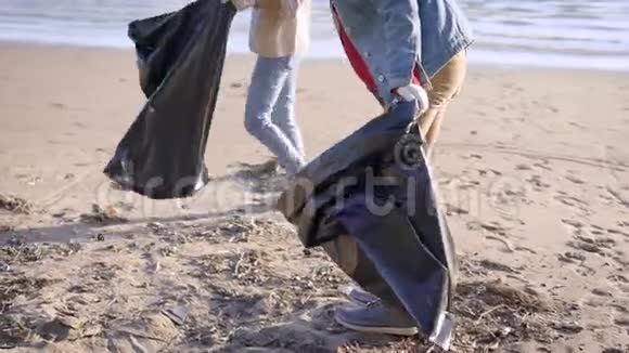 两名女志愿者在春天的沙滩上散步从地上收集垃圾放进塑料袋视频的预览图