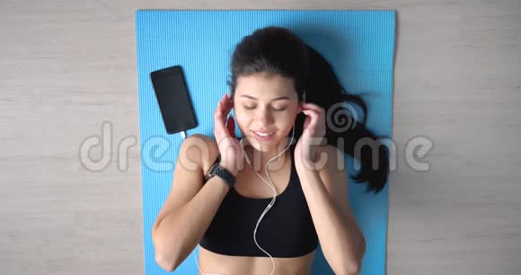 运动女性在瑜伽垫上听耳机音乐视频的预览图