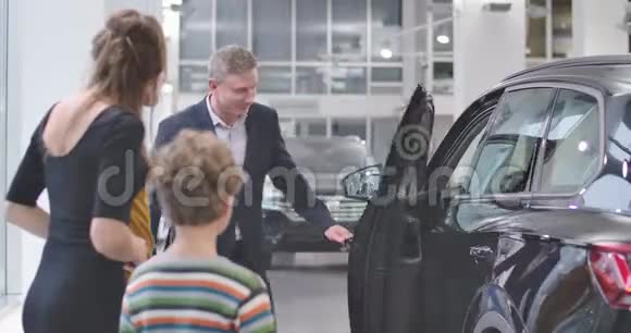 微笑的白种人汽车经销商打开汽车展厅的门年轻留胡子的顾客在沙龙里聊天视频的预览图