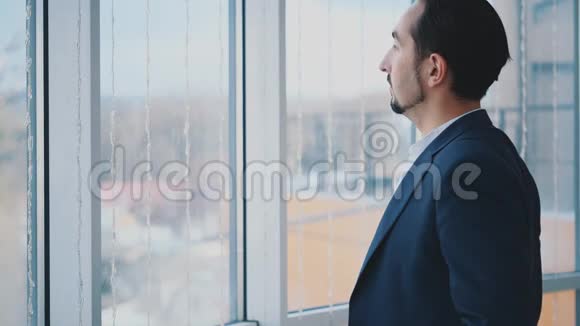 正式套房的商人站在全景窗口前可以看到城市景色严肃的男人侧写视图人类的十字架视频的预览图
