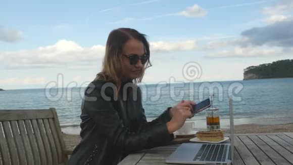 在户外咖啡馆里用笔记本电脑和手机工作的年轻女性视频的预览图