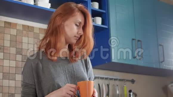 漂亮的红发女孩在家厨房喝早咖啡自由职业者的早晨享受一个困倦的早晨视频的预览图