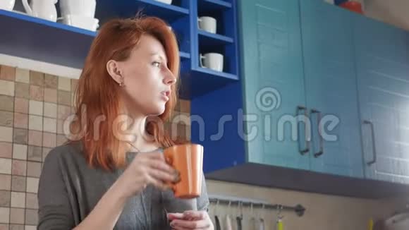 漂亮的红发女孩在家厨房喝早咖啡自由职业者的早晨享受一个困倦的早晨视频的预览图