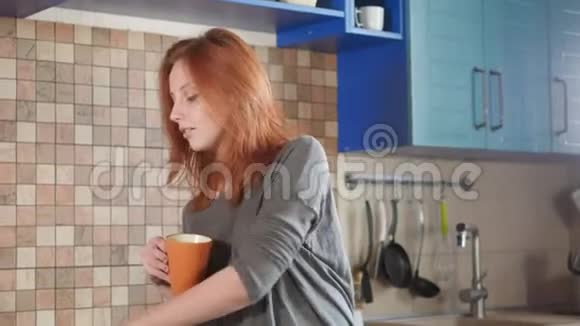 漂亮的红发女孩在家厨房喝早咖啡在智能手机上自拍社交视频的预览图