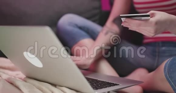 年轻女子的手正坐在沙发上用信用卡在线购买女人用笔记本电脑上网视频的预览图