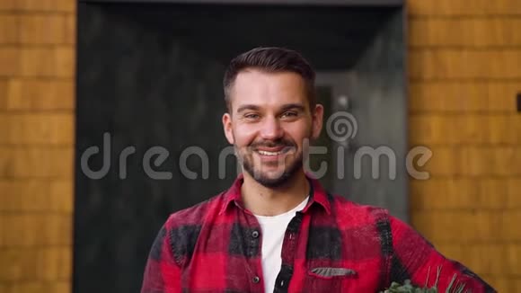 快乐微笑的年轻时尚男士穿着休闲装手里拿着纸盒站在现代住宅附近摆姿势视频的预览图