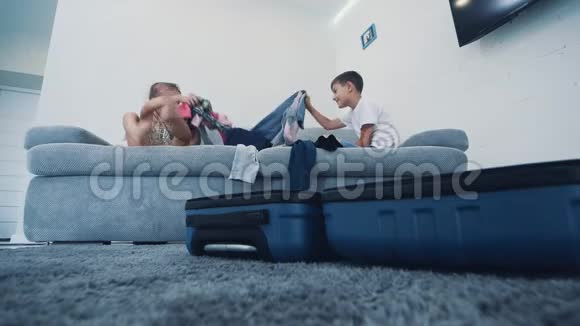 小孩子在家里把衣服扔进手提箱他们坐在蓝色沙发上特写4K视频的预览图
