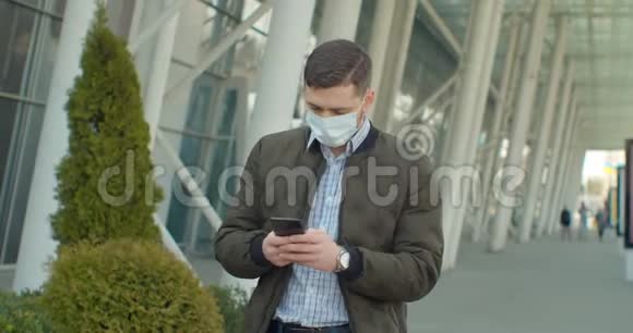 戴防护面罩的青年男子使用手机COVID19冠状病毒感染机场附近流行病毒男性视频的预览图
