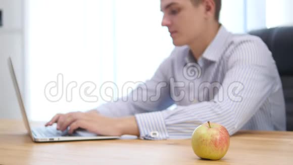 年轻的商人在办公室里咬苹果背景模糊重点是苹果快关门复制空间4K视频的预览图