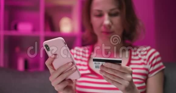 年轻女子坐在客厅的沙发上用信用卡在线购买女性在使用视频的预览图