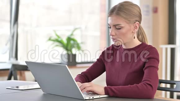背疼的年轻女子在办公室用笔记本电脑视频的预览图