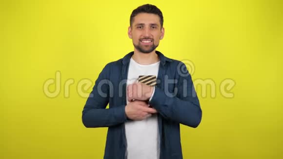 一个穿着白色T恤的年轻人抱着一个着一个盒子看着相机微笑着黄色的背景视频的预览图