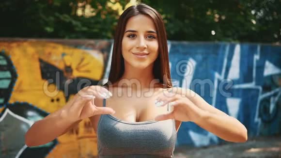快关门性感的健身女孩正在涂鸦背景上展示心脏手势复制空间4K视频的预览图