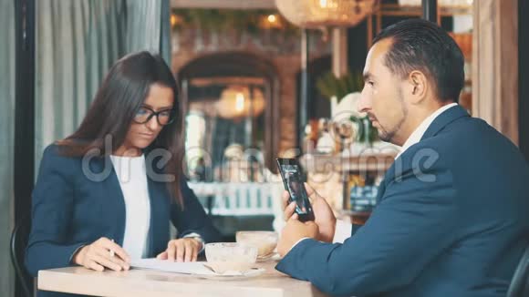 两个商人在一家咖啡馆工作女人正在用心学习文件人在视频聊天侧视关闭视频的预览图