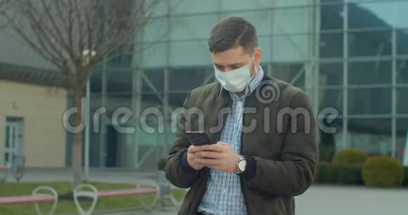 戴防护面罩的青年男子使用手机COVID19冠状病毒感染机场附近流行病毒男性视频的预览图
