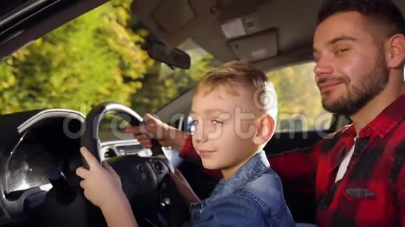 在驾驶课上35岁的大胡子爸爸和可爱的微笑男孩坐在舵手上在摄像机上摆姿势视频的预览图
