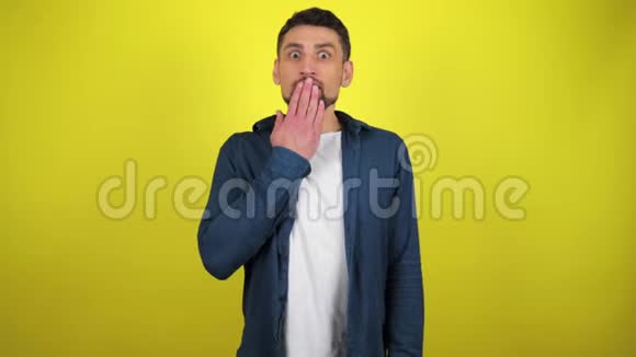 一个穿着蓝色衬衫和白色T恤的年轻人正看着镜头用手掌捂住嘴非常惊讶视频的预览图