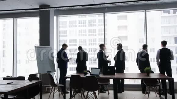 靠在窗户上的人剪影一群年轻的商人在办公室里一起工作和交流视频的预览图
