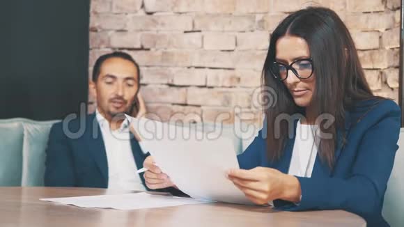 两个商人在一家咖啡馆工作女人正在用心学习文件男人在打电话在模糊视频的预览图