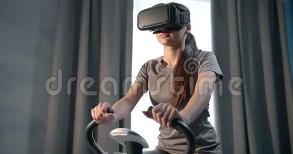 快乐的女人在虚拟眼镜里骑运动自行车做有氧运动视频的预览图