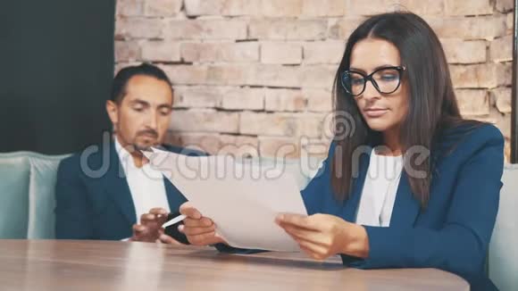 两个商人在一家咖啡馆工作女人正在用心学习文件男人在呼唤某人在模糊视频的预览图