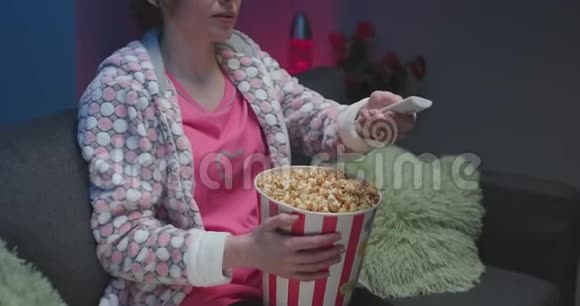 女人在电视上看滑稽电影在沙发上吃爆米花视频的预览图