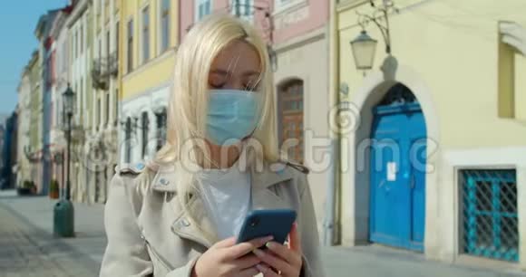 年轻女子戴着防护面具在老城区的街道上使用智能手机担心的女孩搜索关于Covid19的新闻视频的预览图