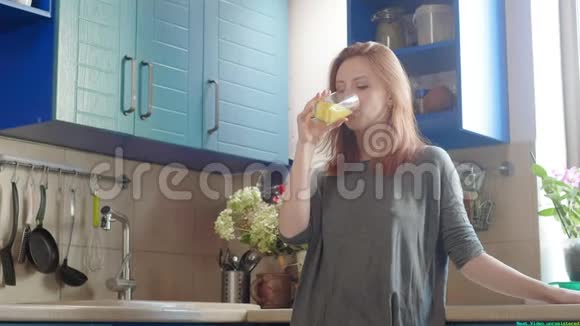 美丽的女孩喝着新鲜的橙汁从玻璃快乐的女人喝水果饮料穿T恤的漂亮女孩视频的预览图