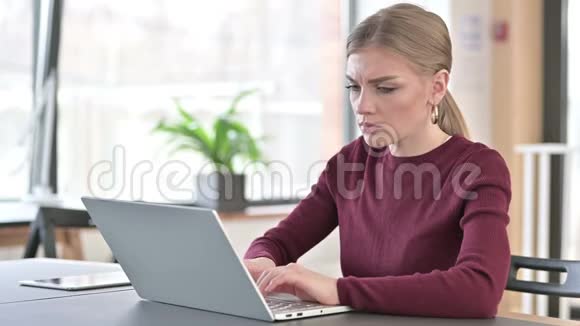 颈部疼痛的年轻女子在办公室使用笔记本电脑视频的预览图