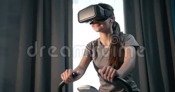 戴着虚拟眼镜在家骑自行车的微笑女人视频的预览图