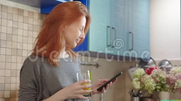 年轻迷人的红发白种人女孩在舒适的厨房里敲击滚动和打字智能手机一个女人视频的预览图