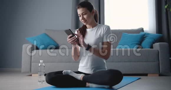 女性在训练后坐在带有智能手机的瑜伽垫上视频的预览图